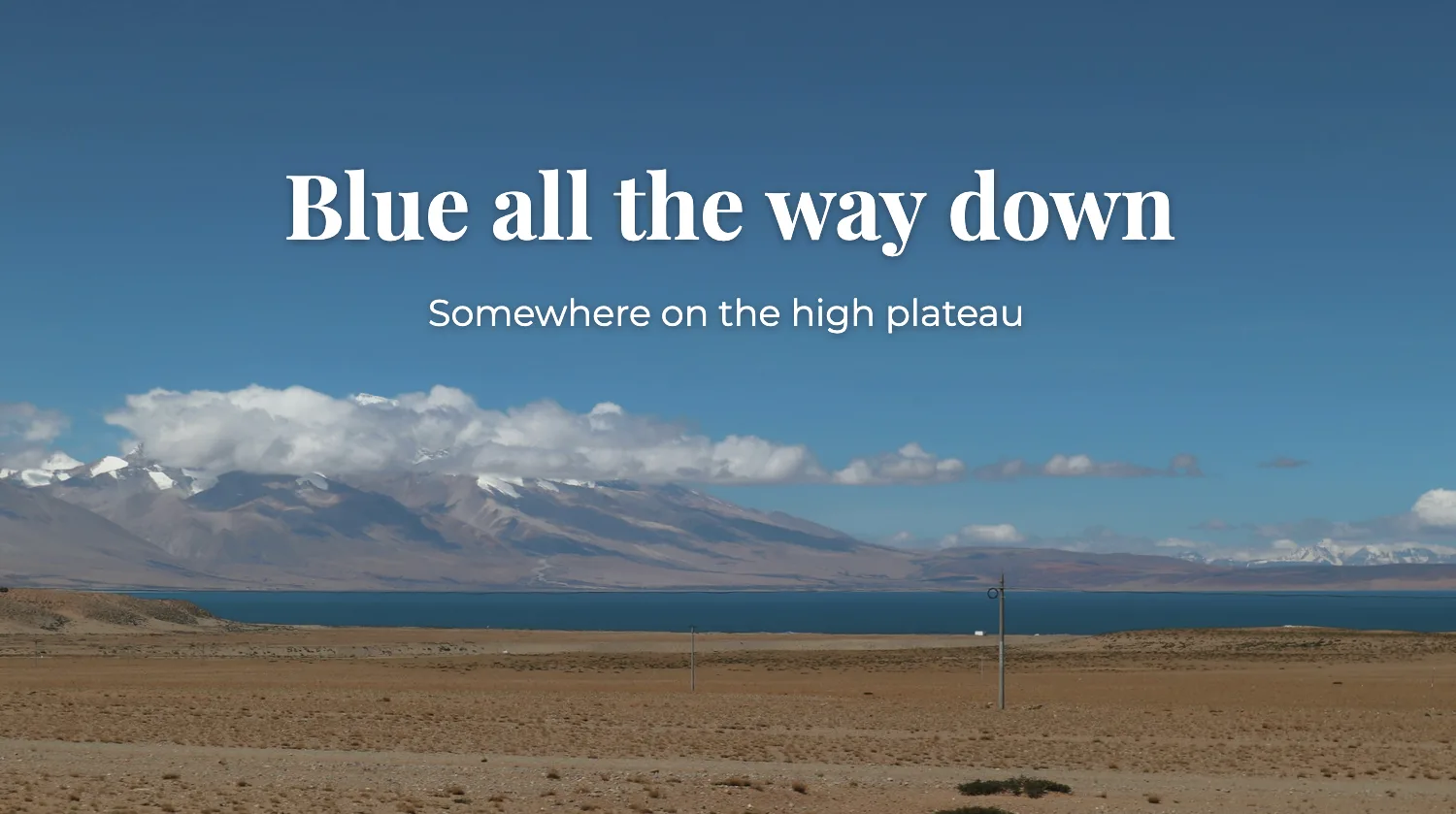 Mountain lake under a blue sky with the caption Blue all the way down added in white serif type